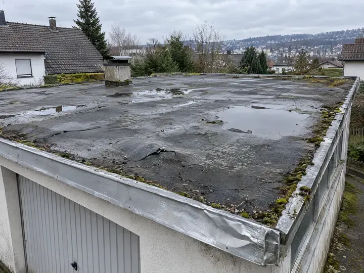 Symbolbild: Flachdach mit blasiger, rissiger Bitumenbahn und stehendem Wasser vor der Sanierung